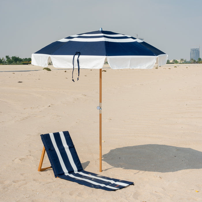 Navy and white striped beach umbrella and beach mat on a sandy beach with a clear sky.