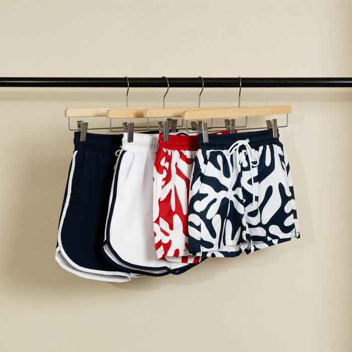 Four pairs of swim shorts hanging on a rack against a beige wall.
