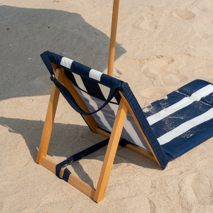 Beach chair with wooden frame and striped blue and white cushion on sand