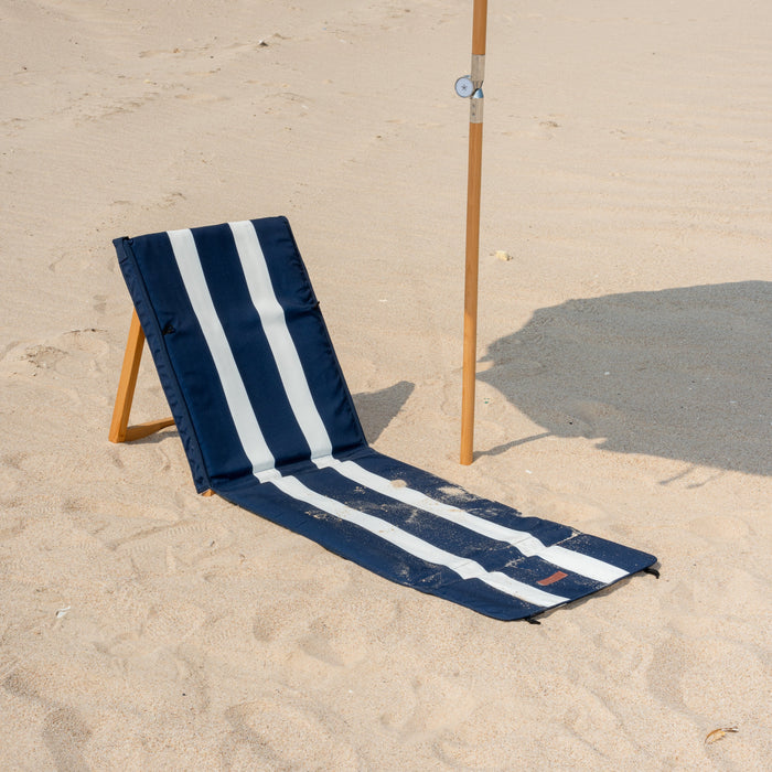 Navy and white striped beach chair on sandy ground with a umbrella in the background