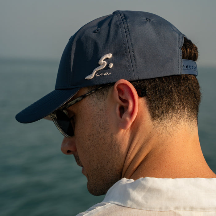 Man wearing a navy cap with a logo, looking out over water.