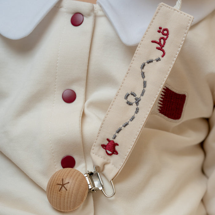 Close-up of a beige baby romper with custom Qatar baby pacifier holder