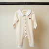 Beige baby romper with white collar and red buttons with embroidered Qatar flag on a hanger against a plain background