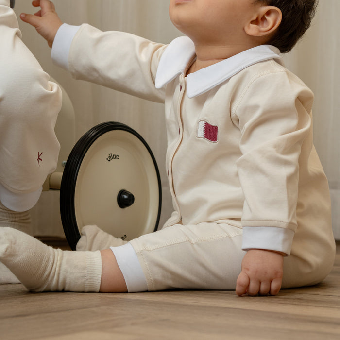 Baby wearing a baby romper with an embroidered Qatar element sitting on the floor