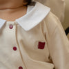 Close-up of a child wearing a custom baby romper with red buttons and a small embroidered Qatar flag patch.