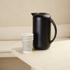Black electric kettle or black vacuum jug on a white surface with an aesthetic background