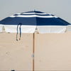 Navy and white striped beach umbrella on a sandy surface with a clear sky.