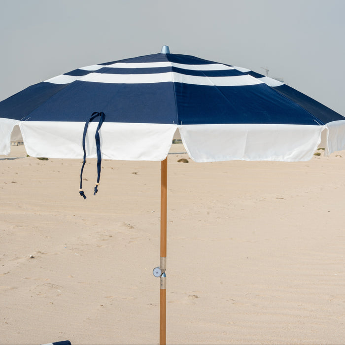 Navy and white striped beach umbrella on a sandy surface with a clear sky.