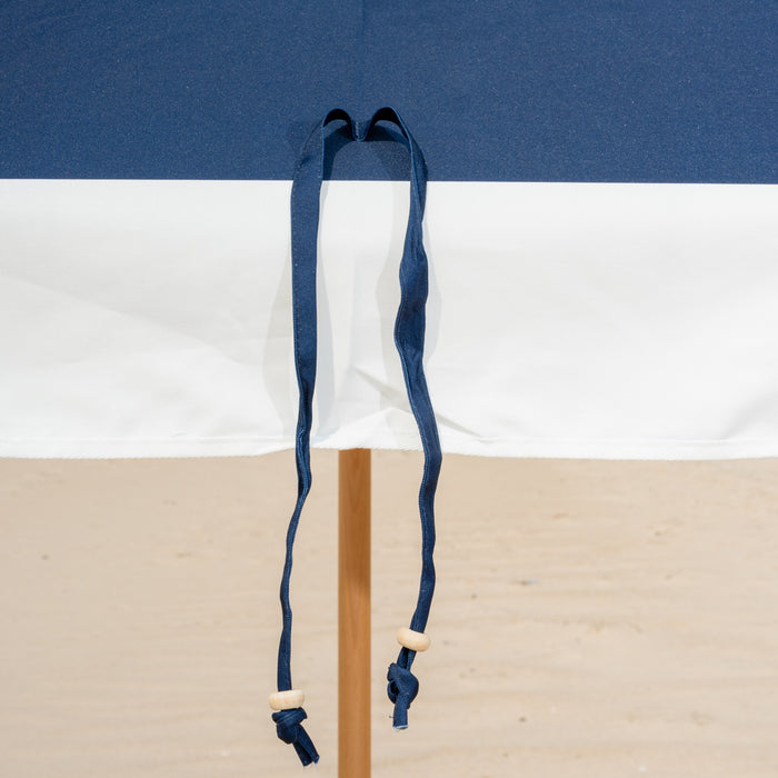Blue and white striped beach umbrella on a wooden stand against a clear blue sky.