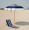 Navy and white striped beach umbrella and beach mat on a sandy beach with a clear sky.