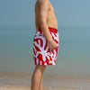 Child wearing red and white swim shorts standing on a beach with clear sky.