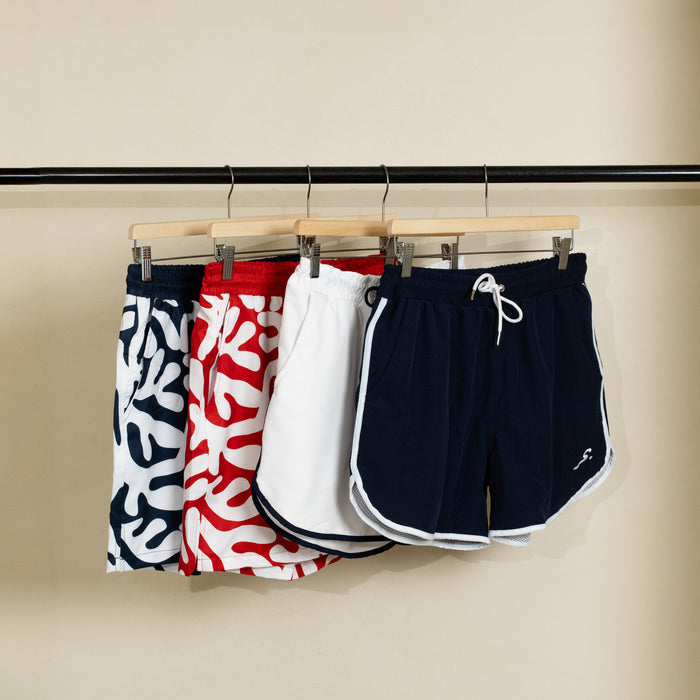 Four pairs of  swim shorts hanging on a rack against a beige wall.