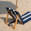 Beach chair with wooden frame and striped blue and white cushion on sand