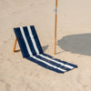 Navy and white striped beach chair on sandy ground with a umbrella in the background