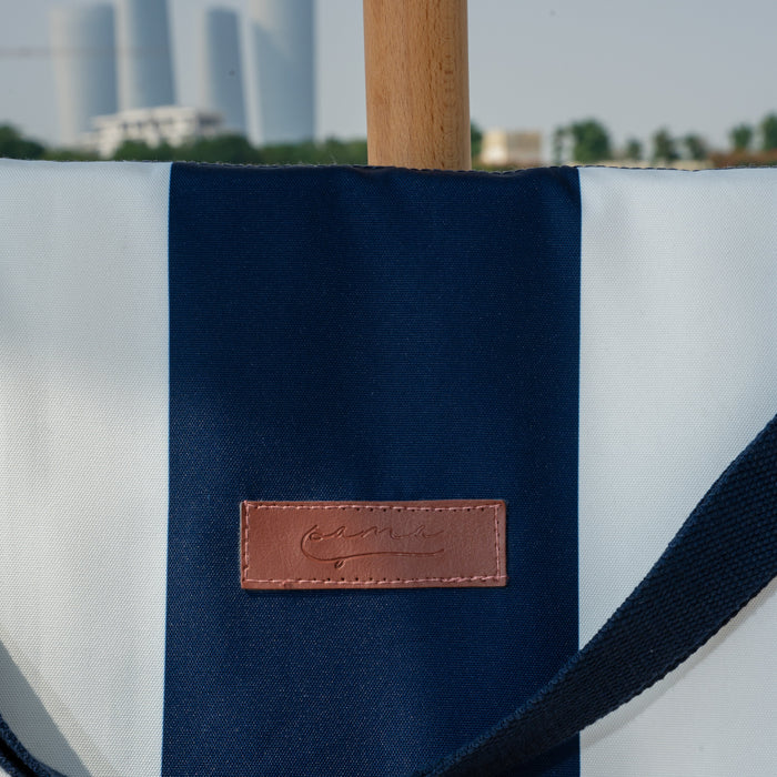 Navy blue and white tote bag with a leather patch on a blurred cityscape background