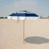 Navy and white striped beach umbrella on a sandy beach with a clear sky.