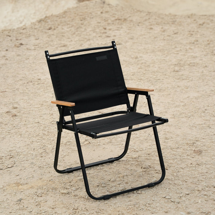 Black folding chair with wooden armrests on a sandy surface