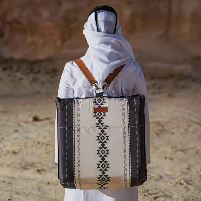 Person in traditional attire thoub carrying a  Sadu patterned rug in a  backpack bag style in a desert setting