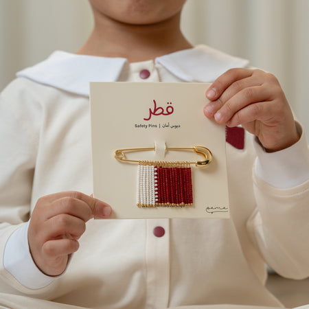 Child holding a card with a brooch Qatar-flag inspired design featuring red, white, and gold colors.