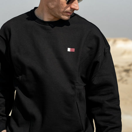Man wearing a black sweatshirt with a small red logo, standing against a neutral background.