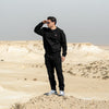 Person wearing Qatar Sweater Trouser Set - Classic Black full set standing on a desert landscape with a plain sky.