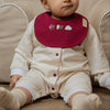 Baby wearing a romper with Qatar baby bib sitting on a beige couch.