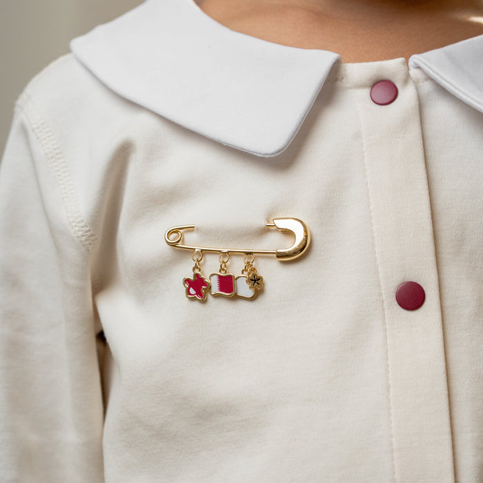 Close-up of a person wearing a white coat with a Qatar charms - baby safety pins