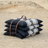Stack of Sadu patterned cushions or pillow with a leather strap on a sandy surface