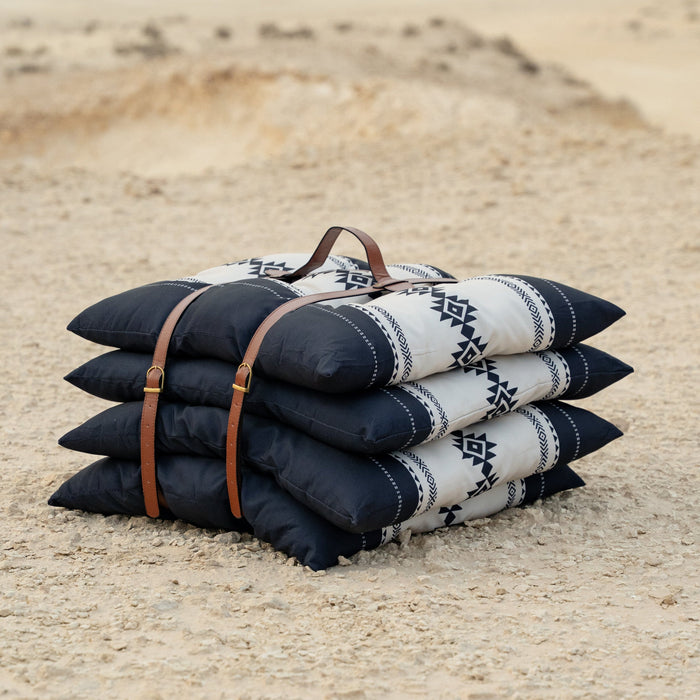 Stack of Sadu patterned cushions or pillow with a leather strap on a sandy surface