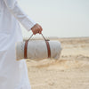 Person holding a rolled-up mat with a strap in a desert setting