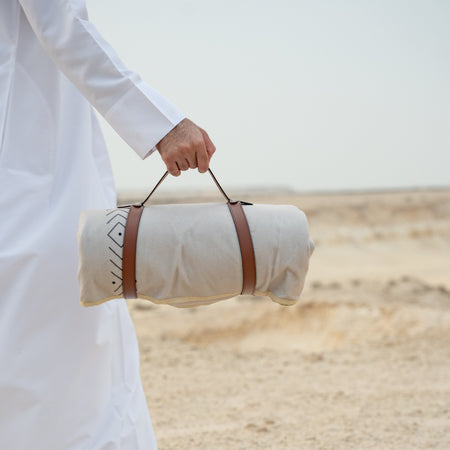 Person holding a rolled-up mat with a strap in a desert setting