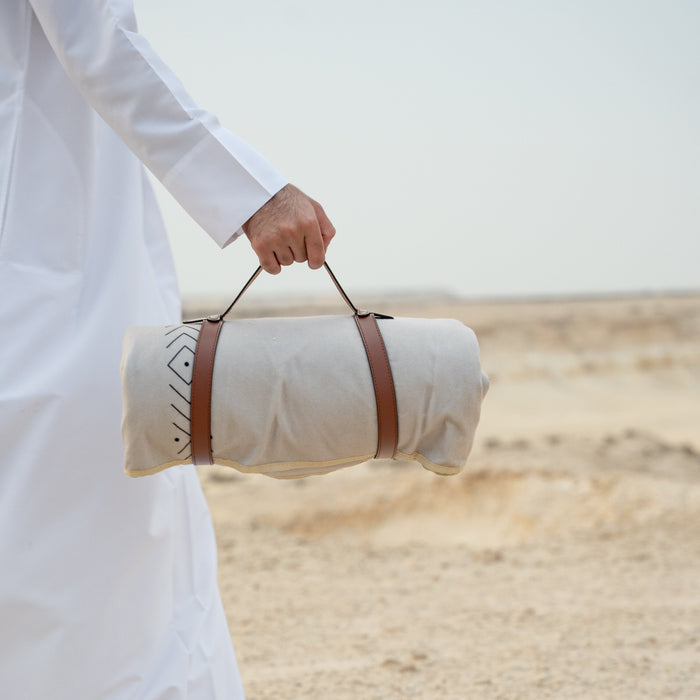 Person holding a rolled-up mat with a strap in a desert setting