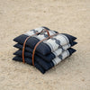 Stack of Sadu patterned pillows or cushions with a brown leather strap on a sandy surface