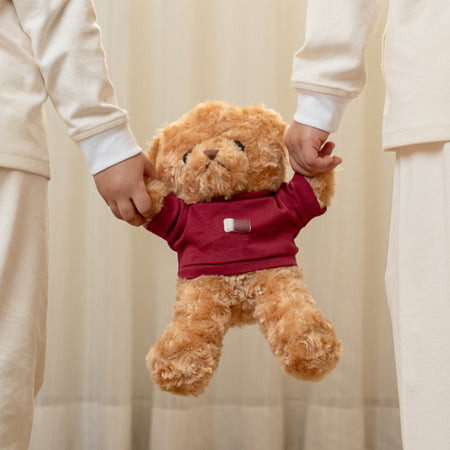 Two children in matching outfits holding a teddy bear with a custom Qatar flag print