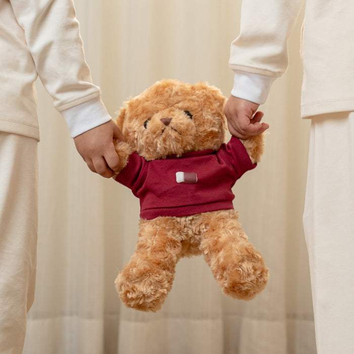 Two children in matching outfits holding a teddy bear with a custom Qatar flag print