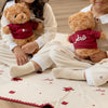 Two children sitting on a decorative rug with teddy bears in a room with white curtains.