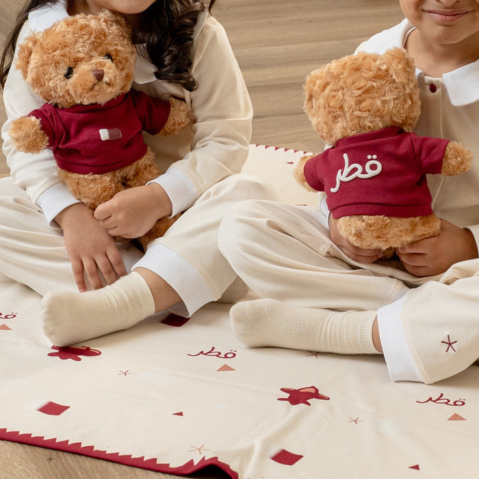 Two children sitting on a decorative rug with teddy bears in a room with white curtains.